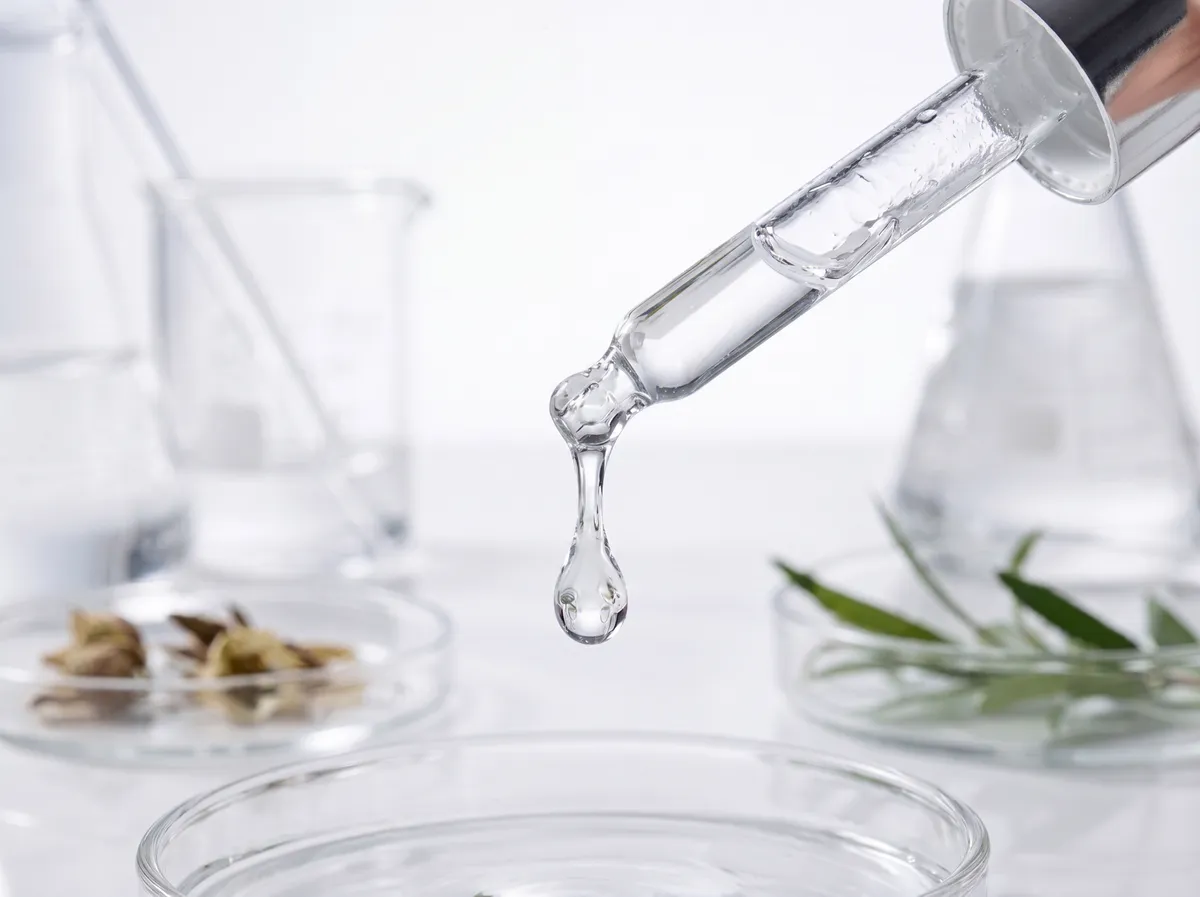 Pipeta z serum nad szkłem laboratoryjnym i zielone liście — naturalne składniki w gabinecie ESTÁ BIEN